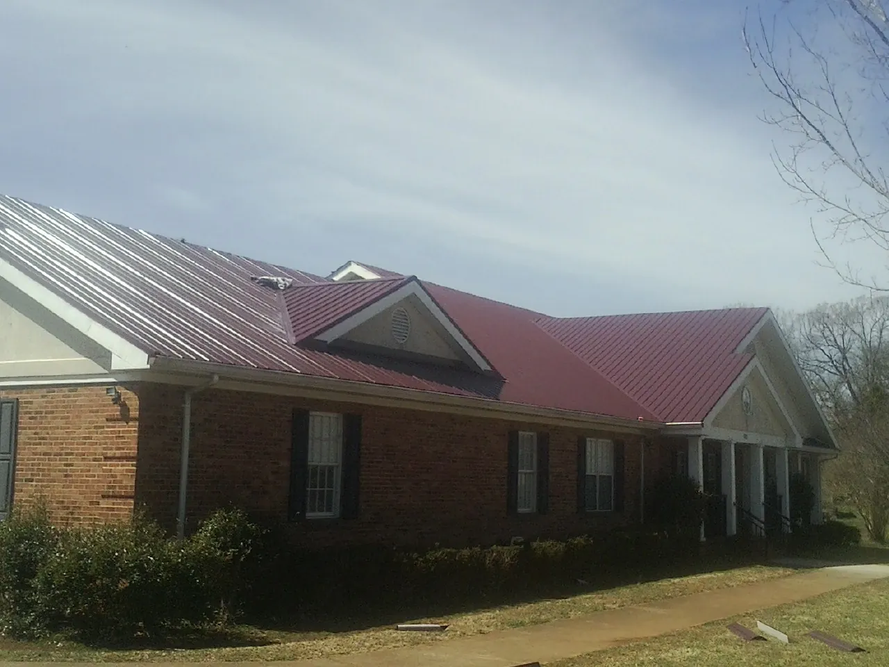 Red metal roof with gabled entries on a long brick building, from a Hail Damage Roof Repair job in French Camp