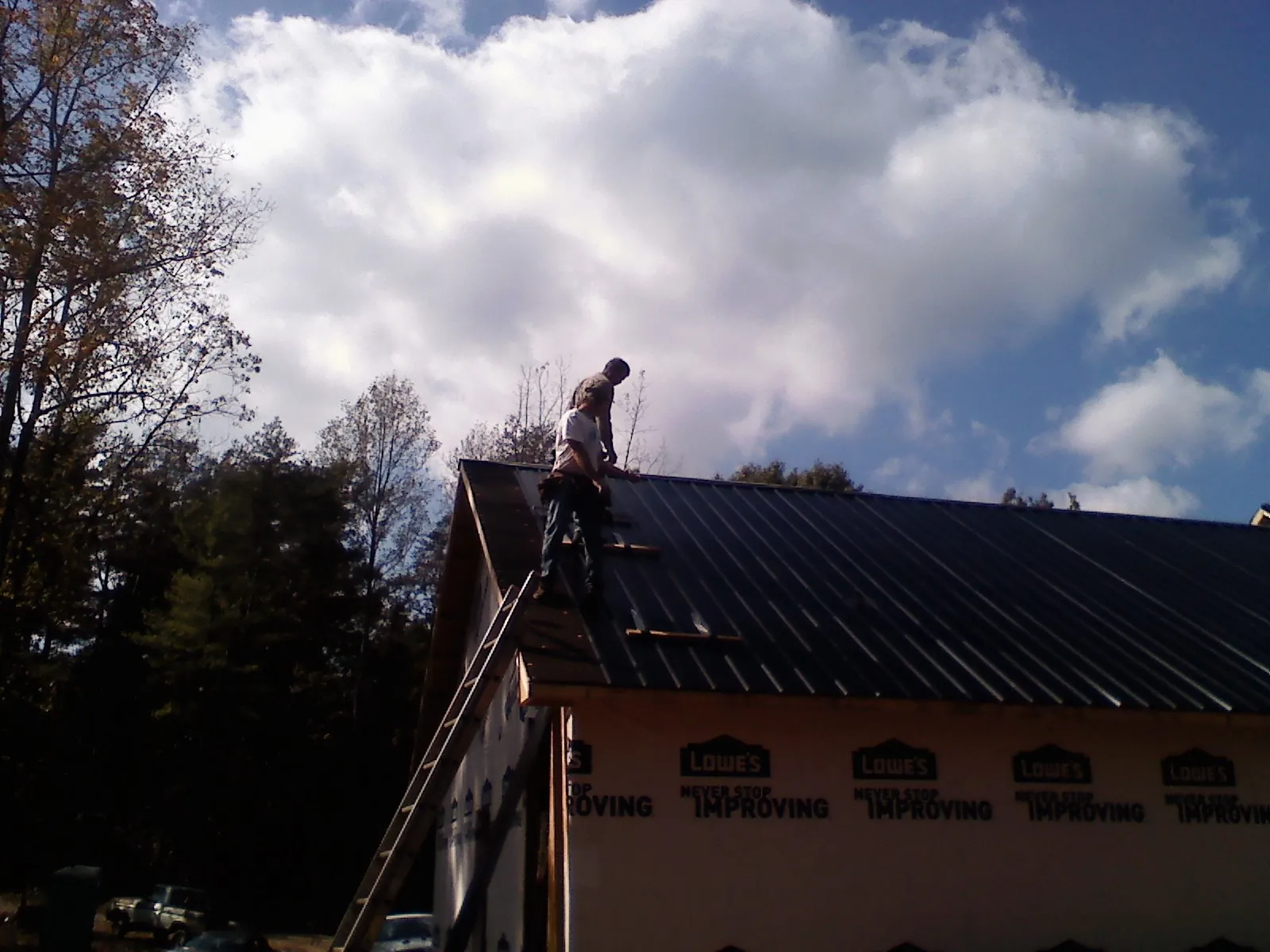 Roofer fastening dark metal panels high against a cloudy sky, from a Roof Inspection job in French Camp